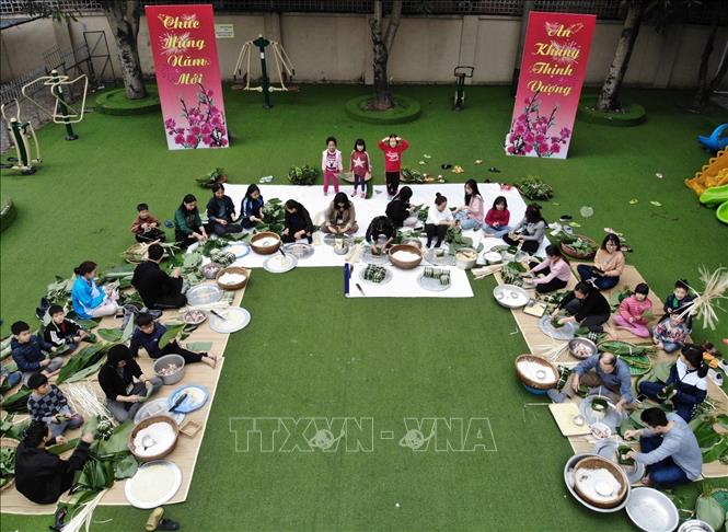 Các mẹ, các con cùng nhân viên của làng gói bánh chưng tết. Ảnh: Hoàng Hiếu - TTXVN 