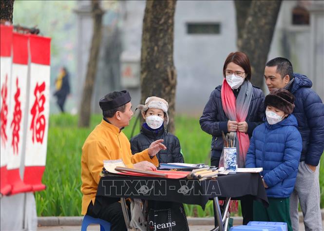 Một gia đình dừng chân bên ông đồ trước cửa đền Ngọc Sơn để nghe giải nghĩa về tục xin chữ đầu năm. Ảnh: Thanh Tùng - TTXVN