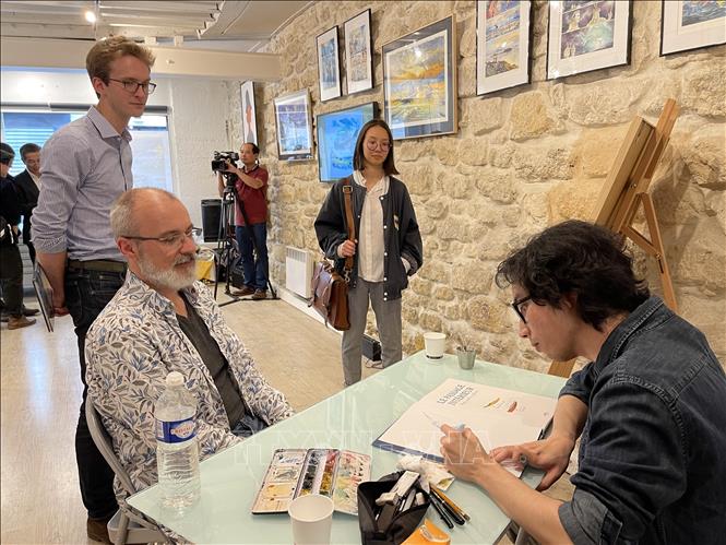 Hoạ sỹ Mai Bách ký tặng sách cho độc giả. Ảnh: Thu Hà  - P/v TTXVN tại Pháp
