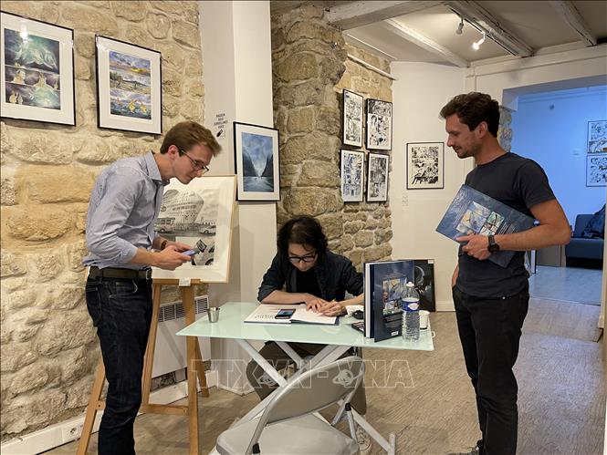 Hoạ sỹ Mai Bách ký tặng sách cho độc giả. Ảnh: Thu Hà  - P/v TTXVN tại Pháp

