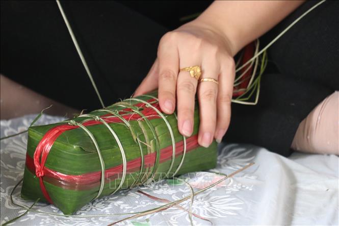 Bánh gói xong dùng dây lạt hoặc dây chuối (xé nhỏ đã phơi nắng cho héo, dai) quấn ngang thân đòn bánh từng sợi như thế năm, mười vòng tùy đòn bánh dài hay ngắn. Ảnh: Chương Đài - TTXVN