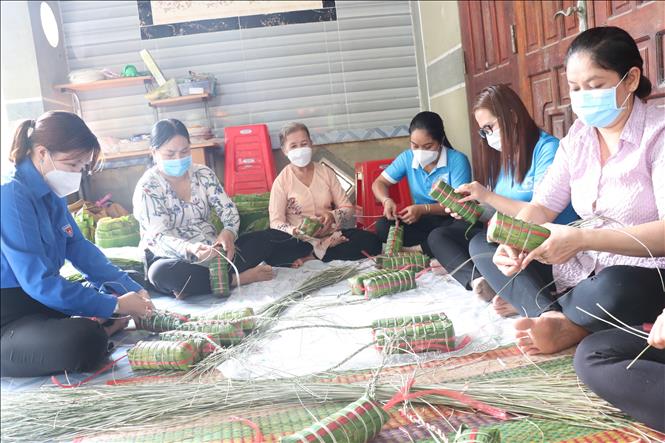 Các bà, các chị quây quần cùng nhau trò chuyện và dùng dây buộc bánh tét sau khi gói để mang đi luộc. Ảnh: Chương Đài - TTXVN