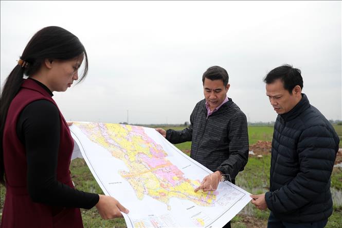 Cán bộ Trung tâm Phát triển Quỹ đất huyện Hoài Đức và xã La Phù nghiên cứu sơ đồ chỉ giới mốc GPMB qua địa bàn xã. Ảnh: Huy Hùng - TTXVN