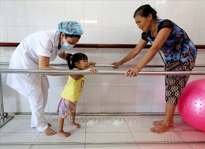Kỹ thuật viên tập phục hội chức năng cho trẻ bị khuyết tật vận động tại Bệnh biện Chỉnh hình và phục hồi chức năng Hà Nội. Ảnh: Anh Tuấn – TTXVN