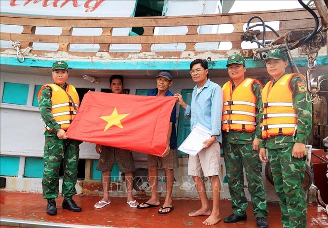 Cán bộ Biên phòng Đồn Biên phòng Sông Đốc trao cờ Tổ quốc cho ngư dân trên tàu đánh bắt xa bờ vùng biển Cà Mau. Ảnh: Hồng Đạt - TTXVN
