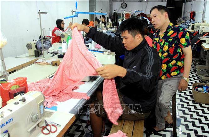 Mặc dù bị khuyết tật bẩm sinh nhưng bằng nghị lực và ý chí vươn lên, ông Phạm Văn Đáp (phải), Giám đốc Công ty TNHH sản xuất và dịch vụ may mặc người khuyết tật ở xã Vũ Lễ, huyện Kiến Xương, tỉnh Thái Bình đã vượt qua khó khăn, vươn lên làm giàu và tạo việc làm cho những người cùng cảnh ngộ. Ảnh: Thế Duyệt – TTXVN