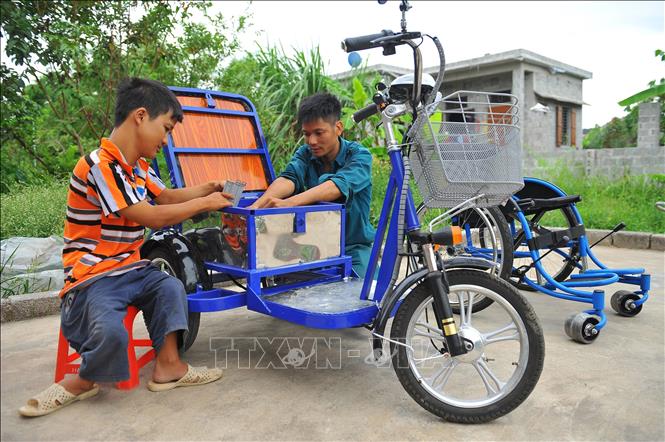 Không may bị dị tật bẩm sinh, khó khăn trong việc đi lại, nhưng anh Lê Văn Lịch (phải) ở xã Trường Yên, huyện Hoa Lư (Ninh Bình) được nhiều người biết đến với ý chí, nghị lực vươn lên trong cuộc sống, là điển hình làm kinh tế ở địa phương nhờ việc làm xe lăn điện cho người khuyết tật, tạo việc làm cho những người khuyết tật khác. Ảnh: Minh Đức - TTXVN