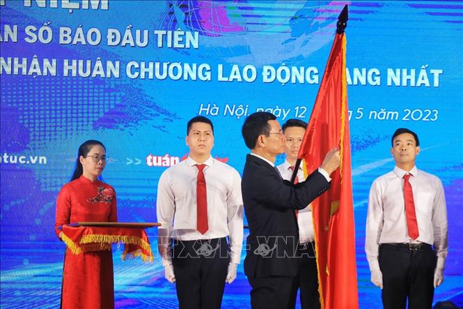 Bộ trưởng Bộ Thông tin và Truyền thông Nguyễn Mạnh Hùng gắn Huân chương Lao động hạng Nhất lên lá cờ truyền thống của Báo Tin tức. Ảnh: Tuấn Anh - TTXVN