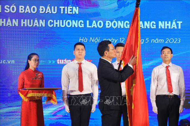 Bộ trưởng Bộ Thông tin và Truyền thông Nguyễn Mạnh Hùng gắn Huân chương Lao động hạng Nhất lên lá cờ truyền thống của Báo Tin tức. Ảnh: Tuấn Anh - TTXVN