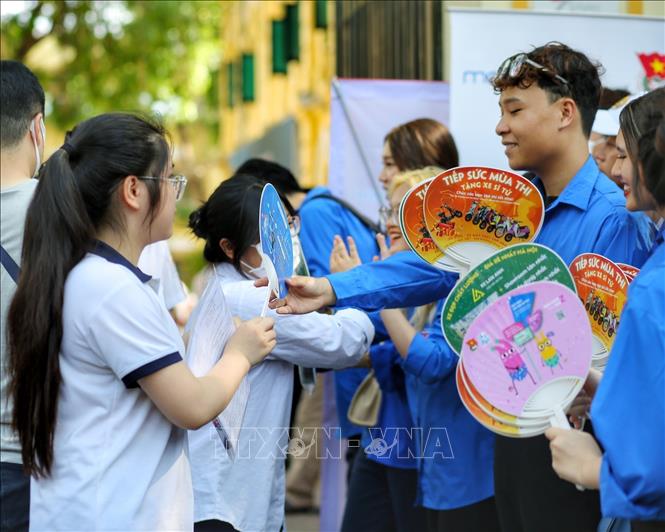 Thanh niên tình nguyện phát quạt cho thí sinh tại điểm thi trường THPT Việt Đức (quận Hoàn Kiếm). Ảnh: Tuấn Đức - TTXVN