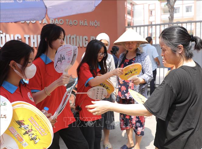 Tình nguyện viên phát quạt cho phụ huynh các thí sinh điểm thi Trường THPT Trương Định. Ảnh: Hoàng Hiếu - TTXVN 