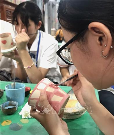 Nữ sinh tỉnh Fukuoka (Nhật Bản) trải nghiệm vẽ hoa văn lên gốm khi tham quan làng nghề Bát Tràng. Ảnh: TTXVN phát