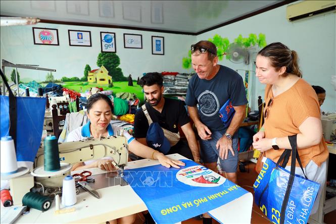 Du khách nước ngoài xem quy trình may các chiếc túi xách từ tấm pano bỏ đi. Ảnh: Đức Hiếu - TTXVN