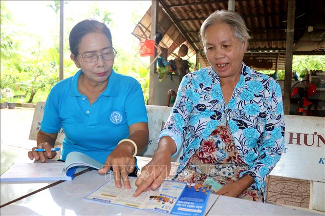 Cán bộ thị trấn Phong Điền, huyện Phong Điền vận động bà Nguyễn Thị Ba tham gia mua bảo hiểm y tế. Ảnh: Thu Hiền - TTXVN