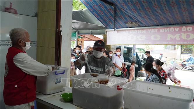 Những tình nguyện viên của Hội Chữ thập đỏ Vòng Tay nhân ái đang phát cơm 0 đồng tại quán gần cổng Bệnh viện Đa khoa Kiên Giang. Ảnh: Văn Sĩ -TTXVN              
 