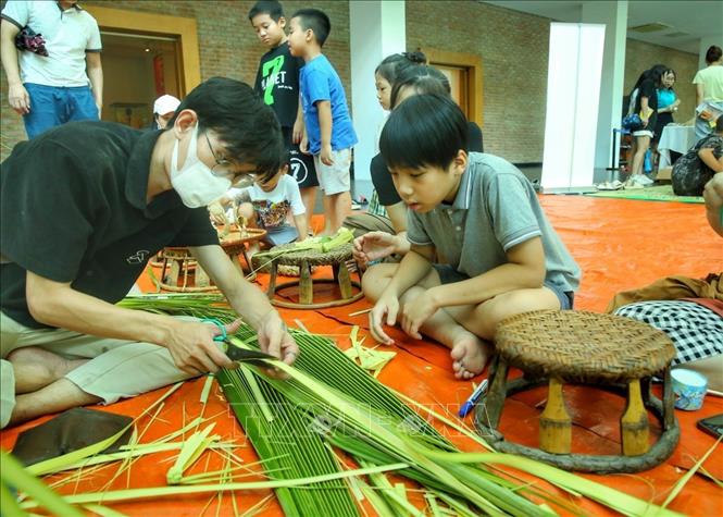 Các em nhỏ xem làm đồ chơi bằng lá. Ảnh: Tuấn Đức - TTXVN
