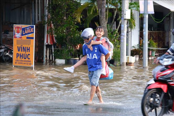 Một người đàn ông bỏ xe máy, cõng con vượt qua đoạn ngập trên đường Nguyễn Văn Cừ, quận Ninh Kiều (Cần Thơ). Ảnh: Thanh Liêm - TTXVN