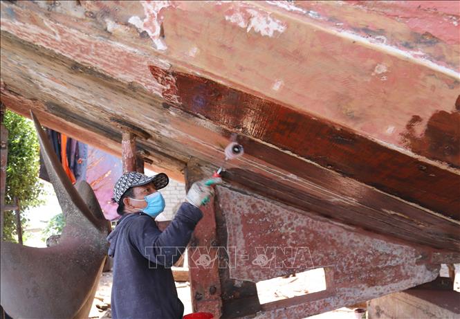 Người thợ quét lớp dầu bóng lên vỏ thân tàu. Ảnh: Xuân Tiến - TTXVN 