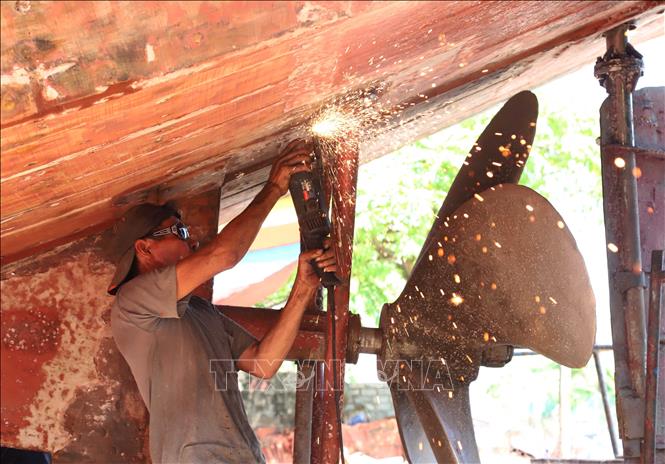 Người thợ dùng máy mài để chà nhám, làm sạch rỉ sắt, mảng bám hệ thống chân vịt cho tàu công suất lớn. Ảnh: Xuân Tiến - TTXVN 