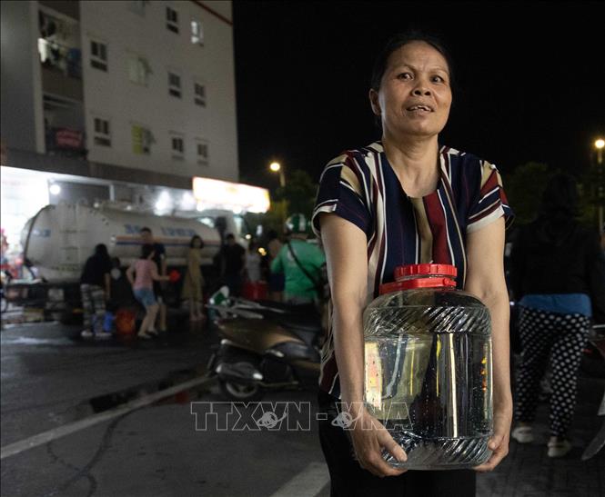 Người dân khu đô thị Thanh Hà tận dụng mọi vật dụng sẵn có để lấy nước từ xe về gia đình. Ảnh: Hoàng Hiếu - TTXVN