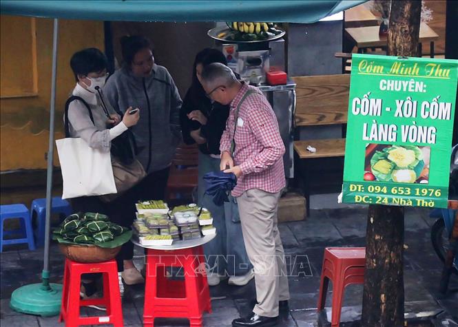 Du khách Nhật Bản tò mò với món cốm, xôi cốm làng Vòng bán trên phố Nhà Thờ. Ảnh: Vũ Thanh - TTXVN phát