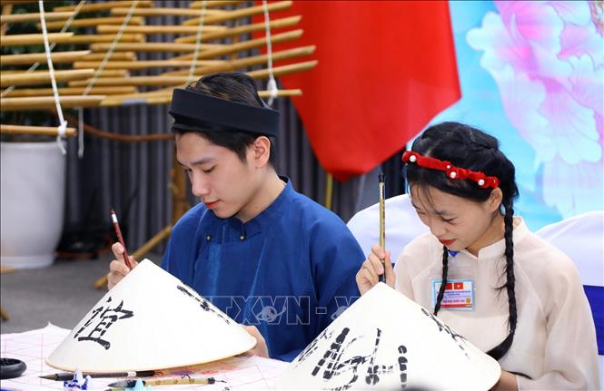 Sinh viên Đại học Quốc gia Hà Nội viết chữ trên nón lá truyền thống Việt Nam để gửi tặng hai Phu nhân. Ảnh: Văn Điệp - TTXVN