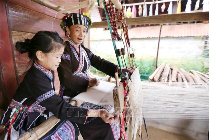 Children learn the art of brocade weaving from a young age by staying near the loom and watching the skillful hands of adults. VNA Photo: Quý Trung