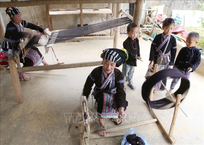 Lu women gather to make brocade fabric, one spins the thread, the other weaves with her loom. VNA Photo: Quý Trung
