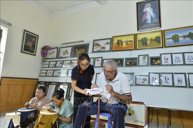 Bà Đinh Thị Lâm hướng dẫn du khách nước ngoài đến tham quan, trải nghiệm và học tập nghề thêu ren. Ảnh: Minh Đức - TTXVN