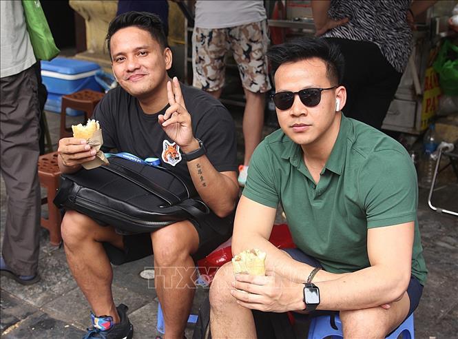 Foreign tourists enjoy banh mi on Hang Can street of Hanoi. VNA Photo