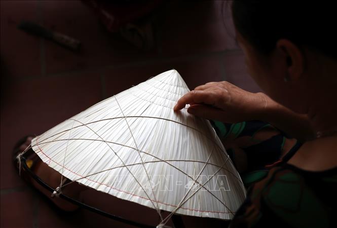 Sewing the leaves into the conical frame requires careful hands and deep attention of artisans. VNA Photo: Hồng Đạt