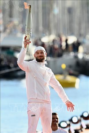 Ca sĩ Pháp JuL giơ cao ngọn đuốc Olympic Paris 2024 trước khi thắp sáng vạc lửa tại buổi lễ ở cảng Marseille ngày 8/5/2024. Ảnh: THX/TTXVN