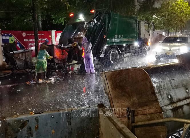 Công nhân vệ sinh môi trường vất vả thu gom rác trong mưa. Ảnh: Thanh Tùng - TTXVN