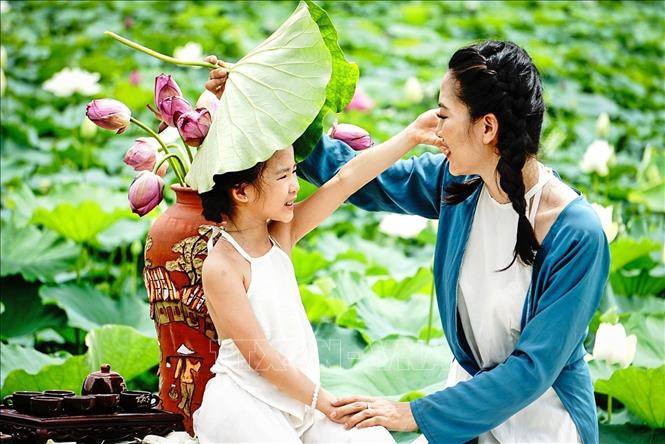 Hai mẹ con bên đầm sen nở sớm ở Hồ Tây (Hà Nội). Ảnh: Khánh Hoà - TTXVN