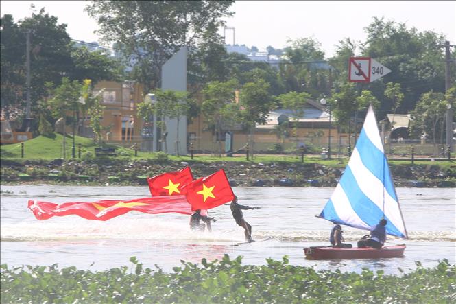 Các vận động viên chuyên nghiệp mang quốc kỳ Việt Nam lướt ván, trên sông Sài Gòn. Ảnh: Thanh Vũ-TTXVN
