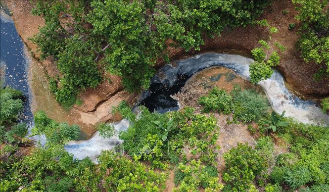 Dòng suối phía sau giáp với nhà máy chế biến mủ cao su L.H ngoài màu đen, bề mặt nước còn nổi lên váng trắng. Ảnh: Đậu Tất Thành – TTXVN
