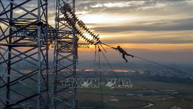Công nhân nhà thầu Công ty CP Tư vấn đầu tư và Xây lắp Điện 5 (PCC5) thi công kéo dây trong ánh hoàng hôn tại vị trí cột 181 tuyến đường dây Nhà máy nhiệt điện Nam Định 1- Phố Nối trên địa bàn huyện Hưng Hà (Thái Bình). Ảnh: Huy Hùng - TTXVN