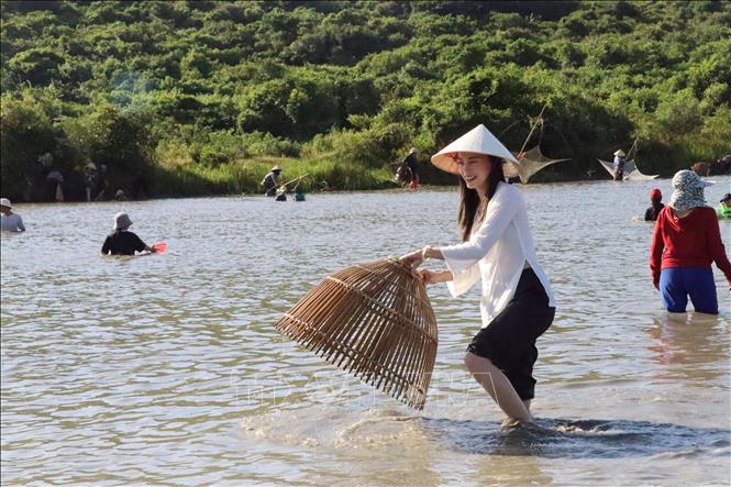 A young girl enjoys catching fish using nom (bell-shaped trapping basket). VNA Photo: Hoàng Ngà