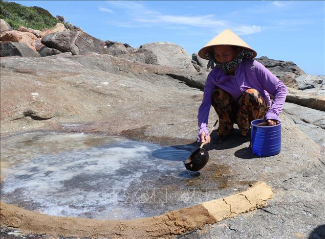 Người dân xóm Cỏ chêm nước biển vào các ô đá kết tinh muối đã được be bờ bằng đất sét để tăng độ dày cho muối. Ảnh: Phạm Cường-TTXVN