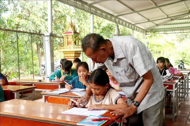 Ông Thạch Hoàng Anh kiểm tra chữ viết của học trò tại lớp dạy chữ Khmer ấp Thới Trường 2, xã Thới Xuân. Ảnh: Thu Hiền - TTXVN