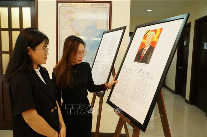 Hai đảng viên trẻ Mai Thùy Dương (bên trong) và  Trần Thị Thanh Tâm (bên ngoài) chăm chú đọc tiểu sử của Tổng Bí thư Nguyễn Phú Trọng tại lễ viếng được tổ chức tại Đại sứ quán Việt Nam tại Malaysia. Ảnh: Hằng Linh-PV TTXVN tại Kuala Lumpur                        