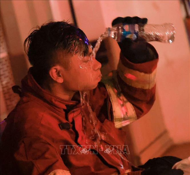 Một chiến sĩ phòng cháy tự làm mát bằng chai nước sau khi tạm rút ra khỏi khu vực đám cháy. Ảnh: Thanh Tùng - TTXVN