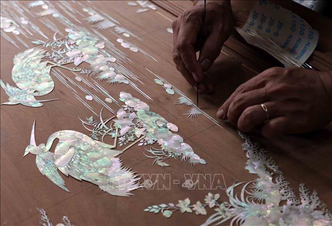 Đặt mẫu trai trên gỗ trước khi đục mảnh. Ảnh: Trần Việt - TTXVN
