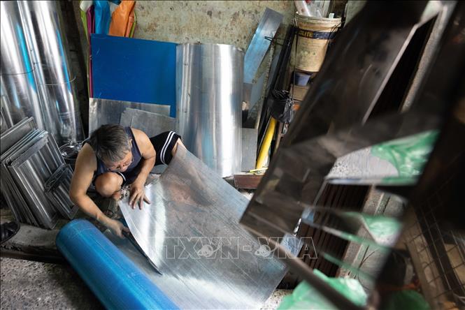 A tinsmith cuts pieces of metal by hands. VNA Photo: Hoàng Hiếu 