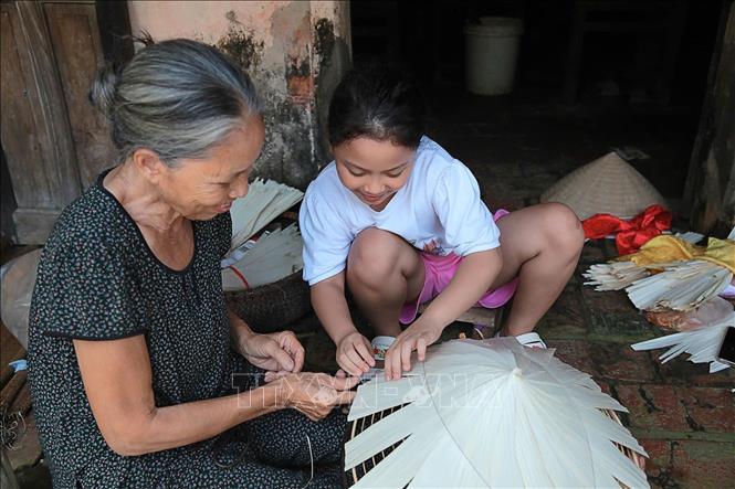 Bà Phạm Thị Liên hướng dẫn cháu gái rải lá trên khuôn. Công đoạn này tuy đơn giản nhưng yêu cầu sự khéo léo và kinh nghiệm để đảm bảo khung nón đều, chắc chắn, và có hình dáng đẹp. Ảnh: Ngọc Liên-TTXVN