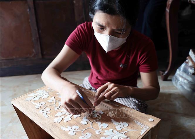 Placing pearl pieces onto wood to trace the outlines before carving. VNA Photo: Trần Việt