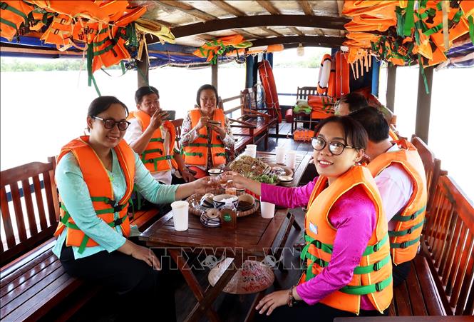 Visitors on a boat tour of Ba Lai river, enjoying “Com Chua Nguyen” (Nguyen lords rice bowl), a local specialty with rice, trai ban (mangrove apple) and fresh fish sauce. VNA Photo: Hồng Đạt