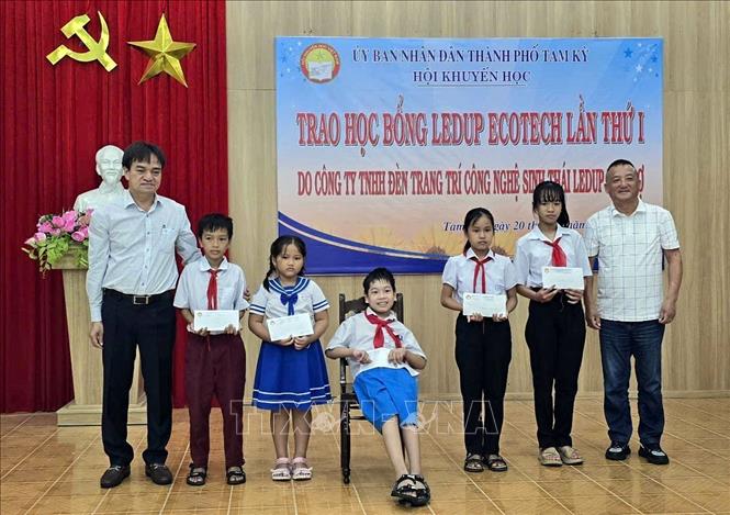 Đại diện nhà tài trợ cùng lãnh đạo thành phố Tam Kỳ trao học bổng cho các học sinh. Ảnh: Trịnh Bang Nhiệm - TTXVN