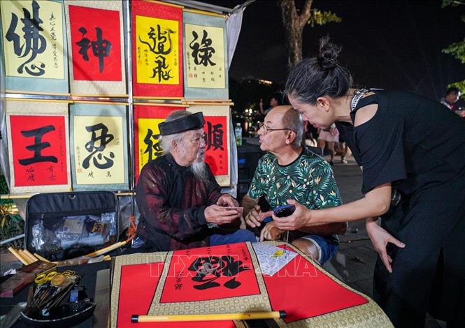 Khách du lịch nước ngoài xin chữ tại phố đi bộ hồ Hoàn Kiếm. Ảnh: Khánh Hòa - TTXVN