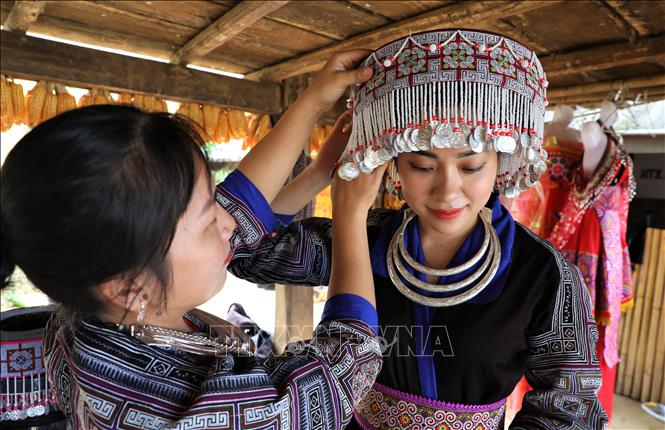 Một du khách được người dân địa phương hướng dẫn cách mặc trang phục của đồng bào Mông. Ảnh: Tuấn Anh – TTXVN 